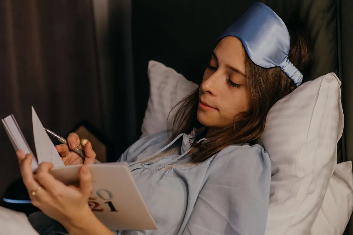 Woman writing in sleep journal while in bed — tracking chronotype and sleep patterns