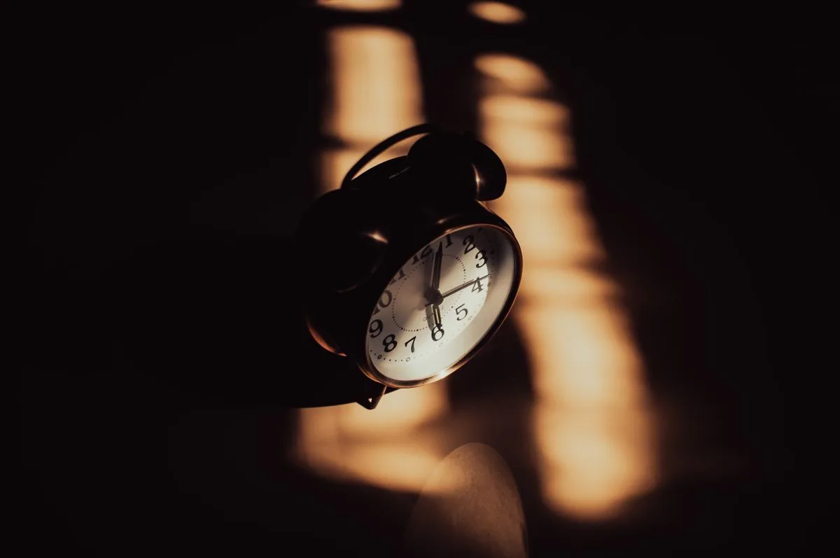 Retro analog alarm clock in moody shadows with warm lighting, representing circadian time