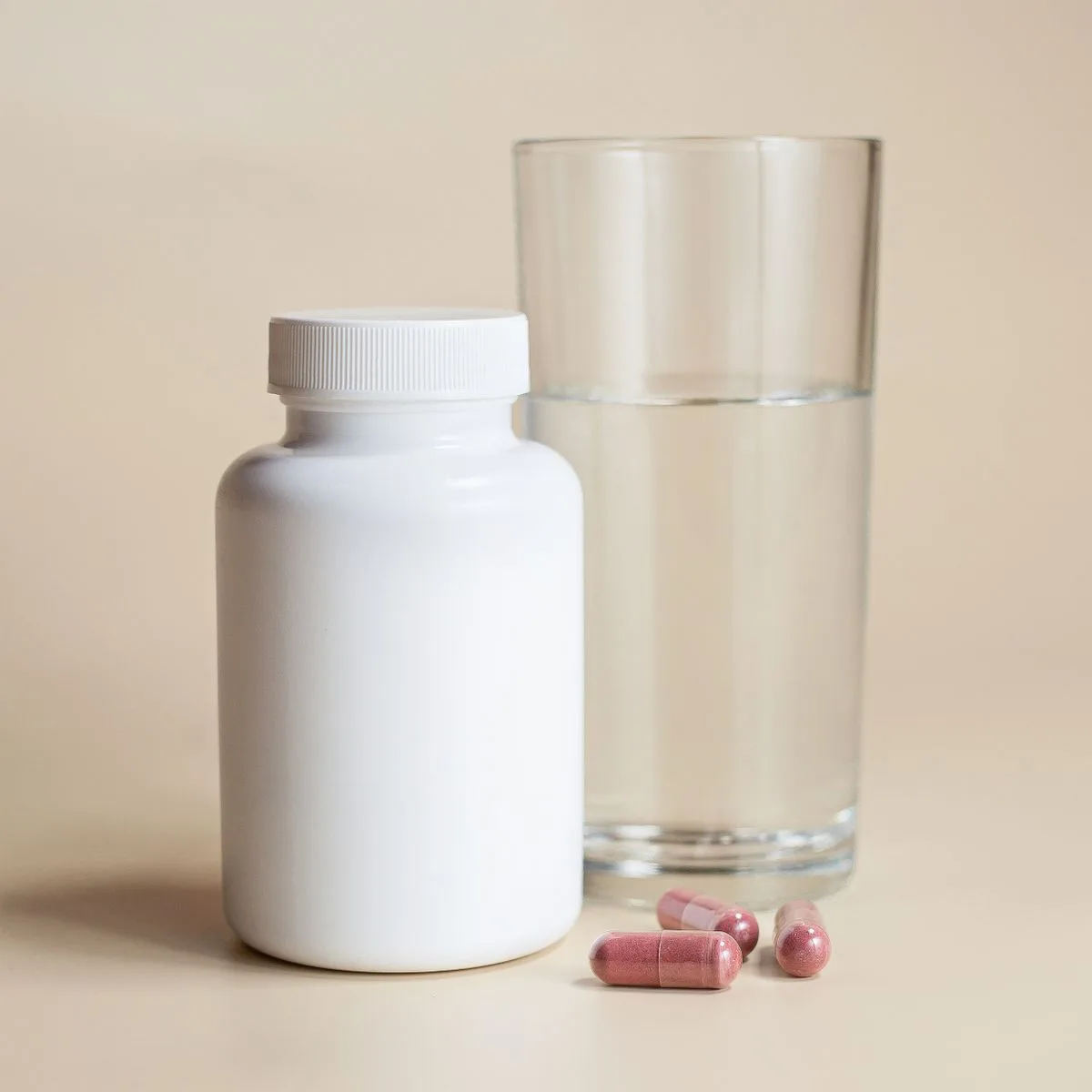 White supplement bottle with capsules and a glass of water on a neutral background