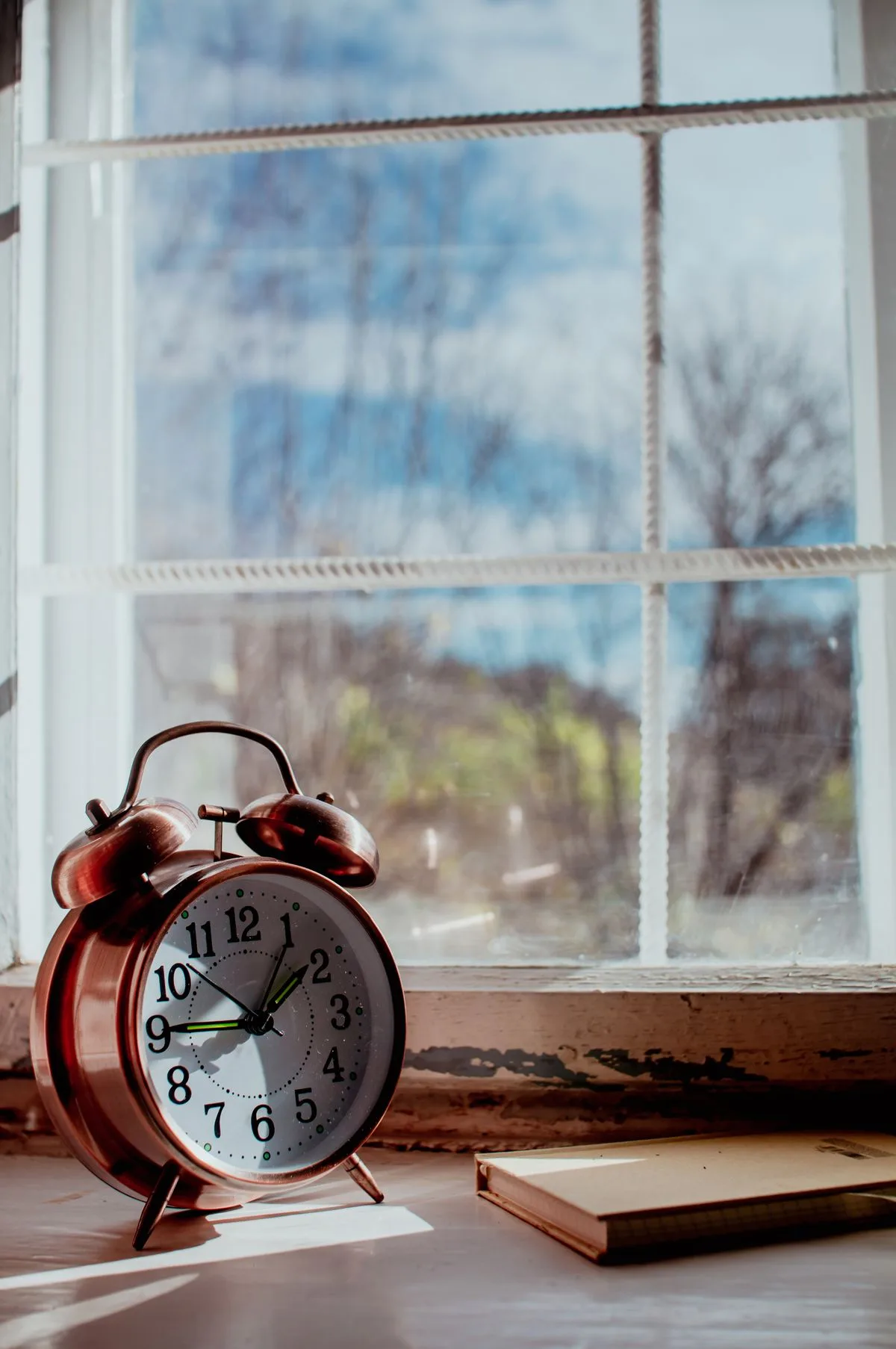 Vintage alarm clock by a sunny window with a notebook, evoking a calm and reflective mood