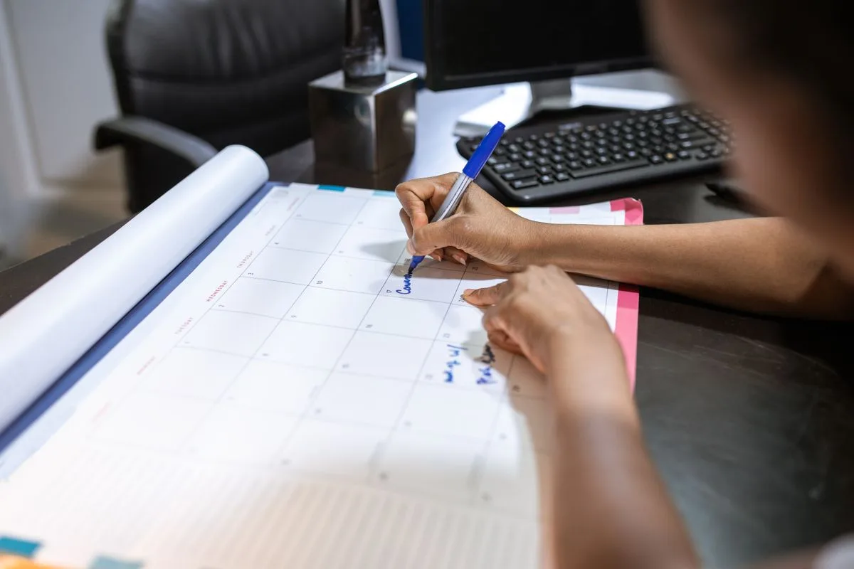 Close-up of a woman planning her schedule on a desk calendar in an office setting