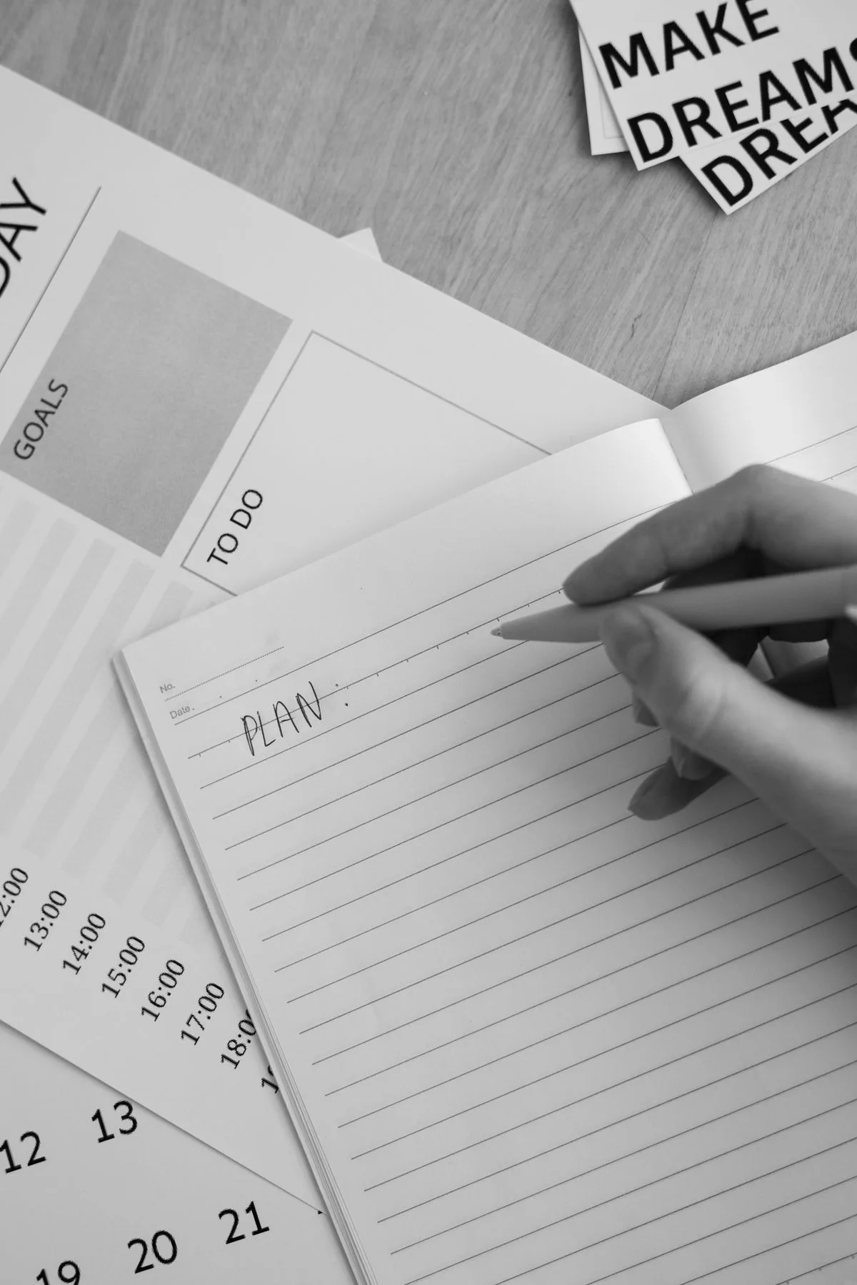 Hand writing 'plan' in notebook with planning materials around