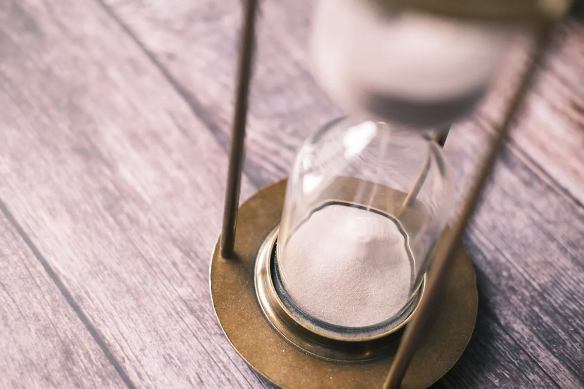 Close-up of a vintage hourglass with sand flowing on a wooden background
