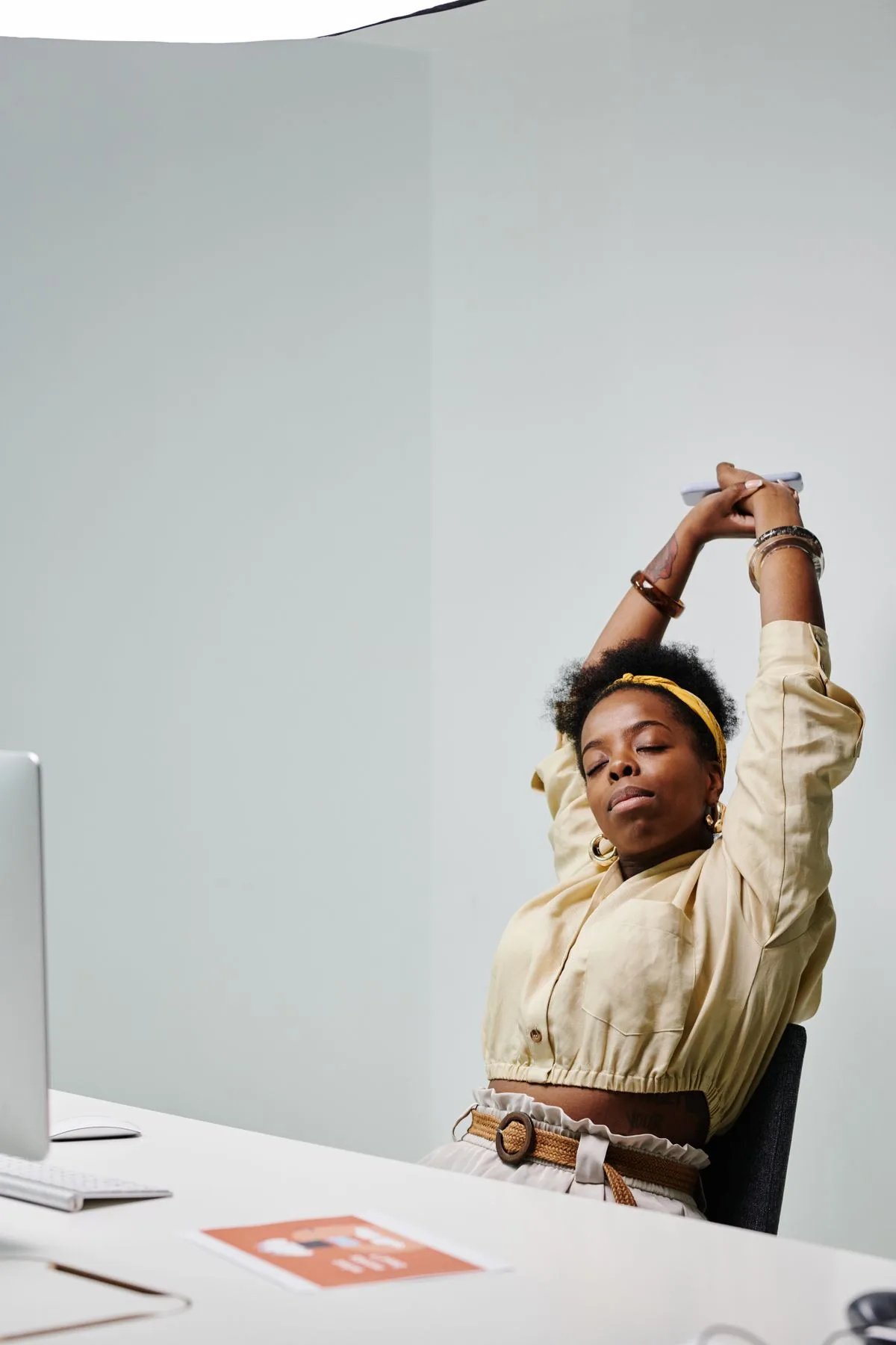 African American woman stretching with eyes closed at her office desk, feeling relaxed
