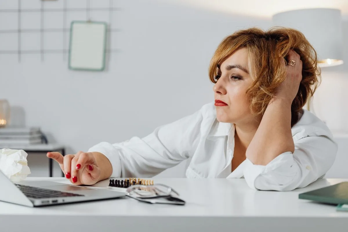 Frustrated woman at desk using laptop with expression of stress, indoors office environment