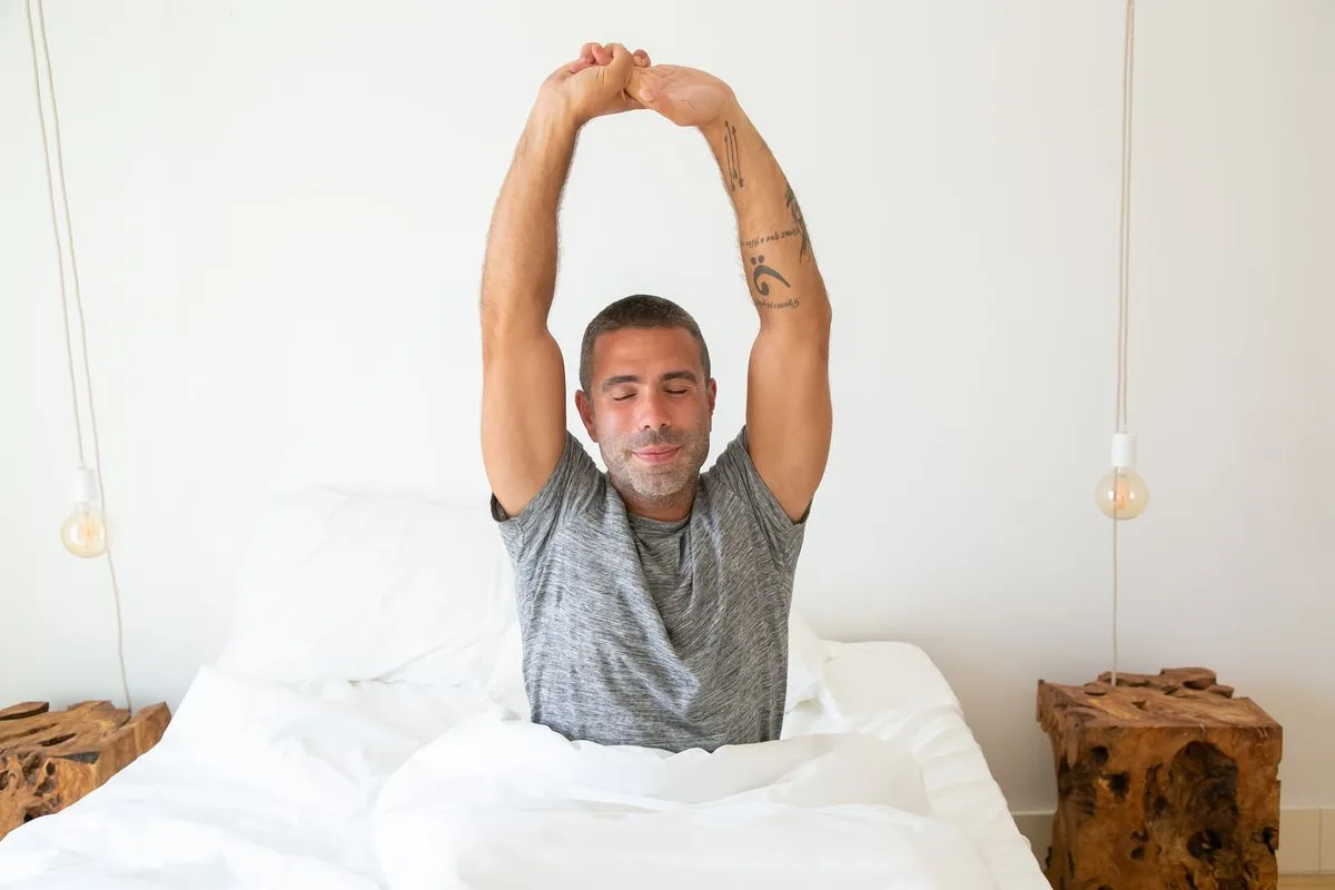 Man stretching arms while waking up in bed — morning cortisol window and energy peak