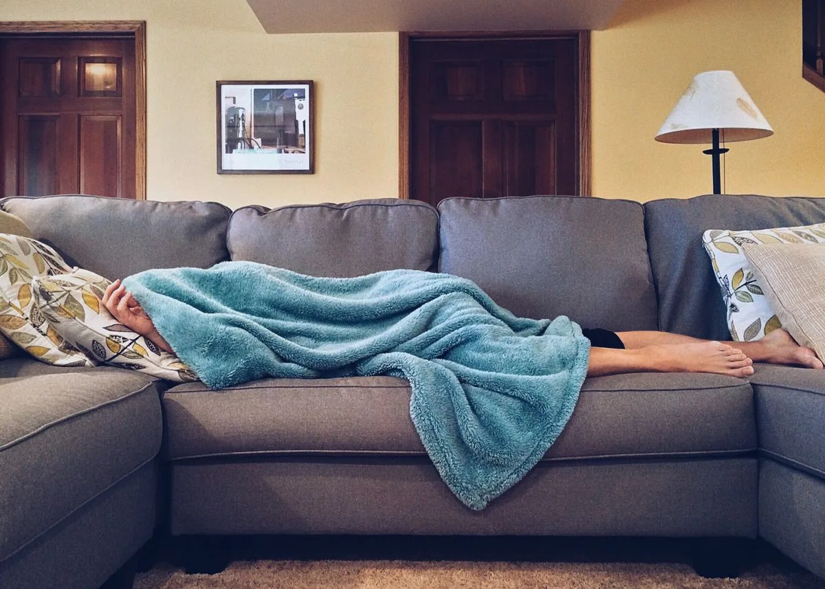 Person resting on couch under blanket — afternoon energy trough and strategic napping